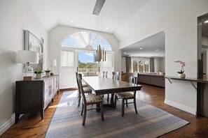 A modern kitchen with a dining area, featuring a large table, chairs, and a view through an arched window.