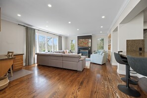A modern living room with hardwood flooring, a sectional sofa, a fireplace, and a dining area with a wooden table and chairs.