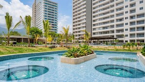 A swimming pool with multiple circular hot tubs, surrounded by palm trees and a large hotel building. - Ideal for Resting! Apartasuite for Couples with Ocean View and Swimming Pools (Santa Marta)