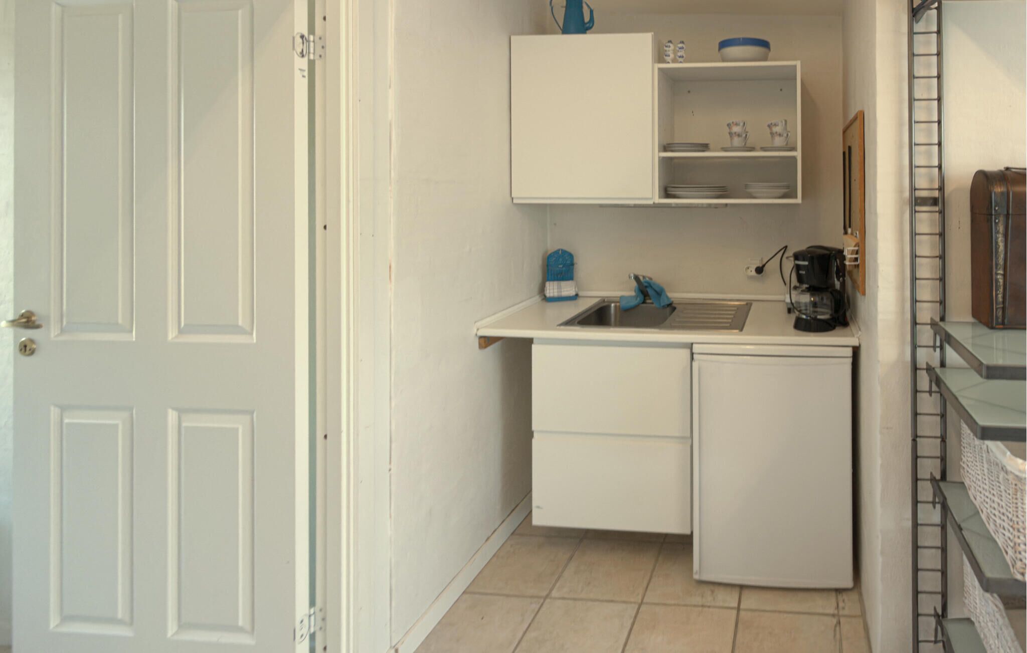 A compact kitchen with a sink, a coffee maker, and a small cabinet.