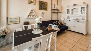 A dining area with a table, chairs, a vase of flowers, a clock, and a sofa in the background.
