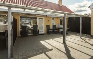 A covered outdoor seating area with chairs and a table, a car parked outside, and a building with a tiled roof.