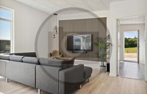 Ein modernes Wohnzimmer mit grauem Sofa, einem Flachbildfernseher an einer Wand mit vertikalen Jalousien, einem Topf mit Pflanze und Blick auf einen Garten durch eine offene Tür.