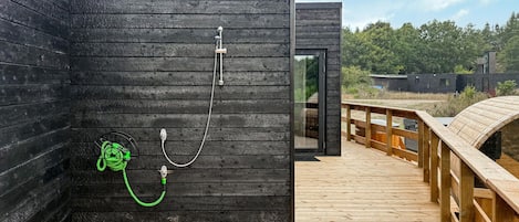 A modern wooden sauna with a glass door, a wooden deck, and a metal railing.