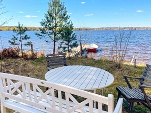 A lakeside deck with a table and chairs, a dock with a boat, and a forested shoreline. - 4 Star Holiday Home in Vaxjo (Växjö)