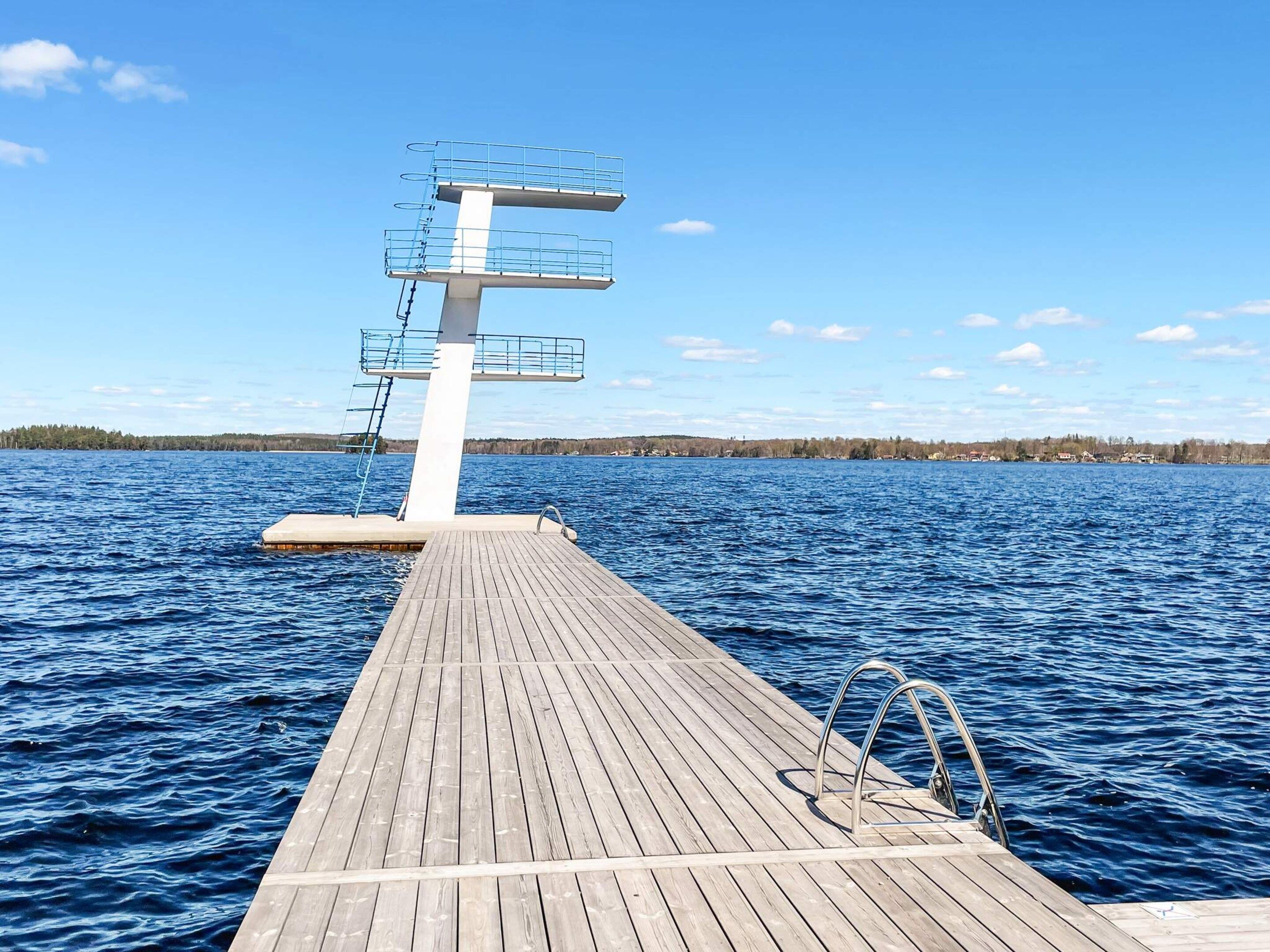 A wooden dock leading to a diving platform with railings, extending into a body of water with a clear sky.