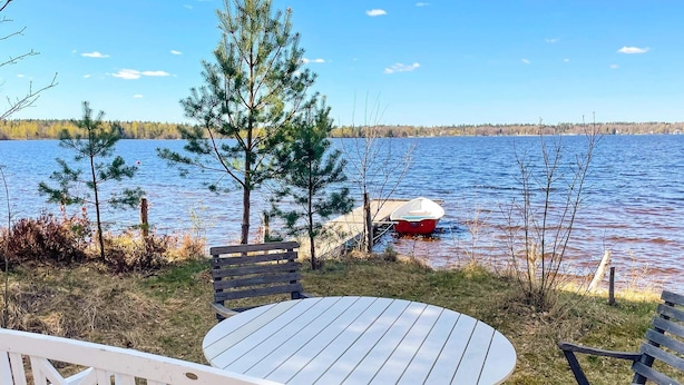 A lakeside deck with a table and chairs, a dock with a boat, and trees in the background. - 4 Star Holiday Home in Vaxjo (Växjö)