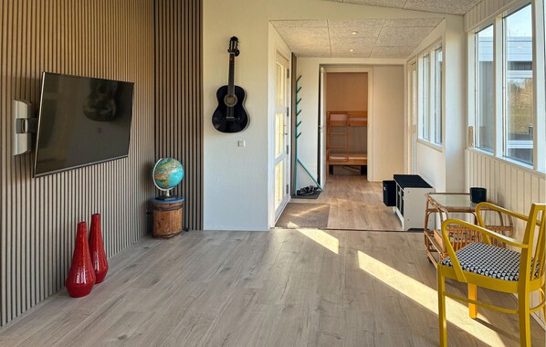 Una sala de estar moderna con televisor, guitarra, un globo terráqueo y un comedor con sillas amarillas.