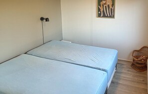 A room with two beds, a wall-mounted lamp, a painting, and a wicker chair. - 3 bedroom awesome home in Juelsminde (Juelsminde)