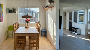 Un comedor con una mesa de madera, sillas, un florero con flores, una lámpara colgante y una ventana con persianas.