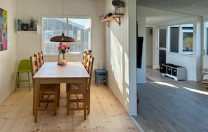 Un comedor con una mesa de madera, sillas, un florero con flores, una lámpara colgante y una ventana con persianas.