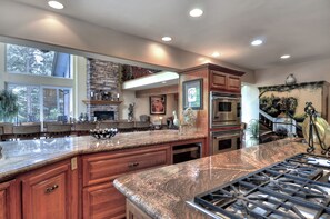 A spacious kitchen with granite countertops, wooden cabinets, a built-in oven, and a large island with a sink. - Grand Oriole Estate (Big Bear Lake)