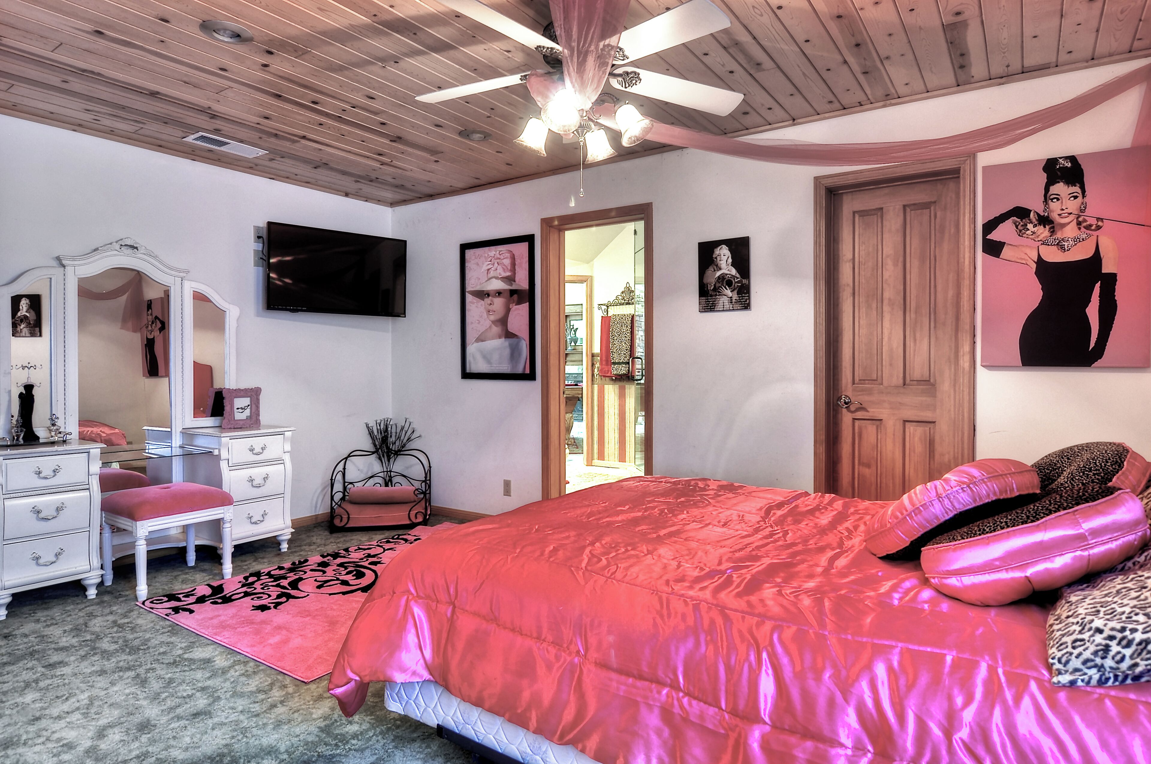 A bedroom with a bed, a vanity, a mirror, a ceiling fan, and a door.