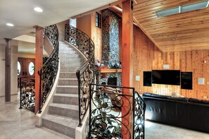 A wooden interior with a spiral staircase, stone wall, and a black leather sofa. - Grand Oriole Estate (Big Bear Lake)