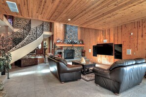 A spacious living area with a stone fireplace, leather sofas, a coffee table, and a TV. - Grand Oriole Estate (Big Bear Lake)