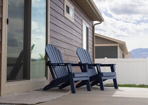 Two Adirondack chairs outside a house with a sliding glass door and a white fence in the background. - Skyview Play and Stay Retreat (Cody)