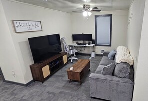Ein Wohnzimmer mit Fernseher, Computertisch, einer Couch und einem Deckenventilator.