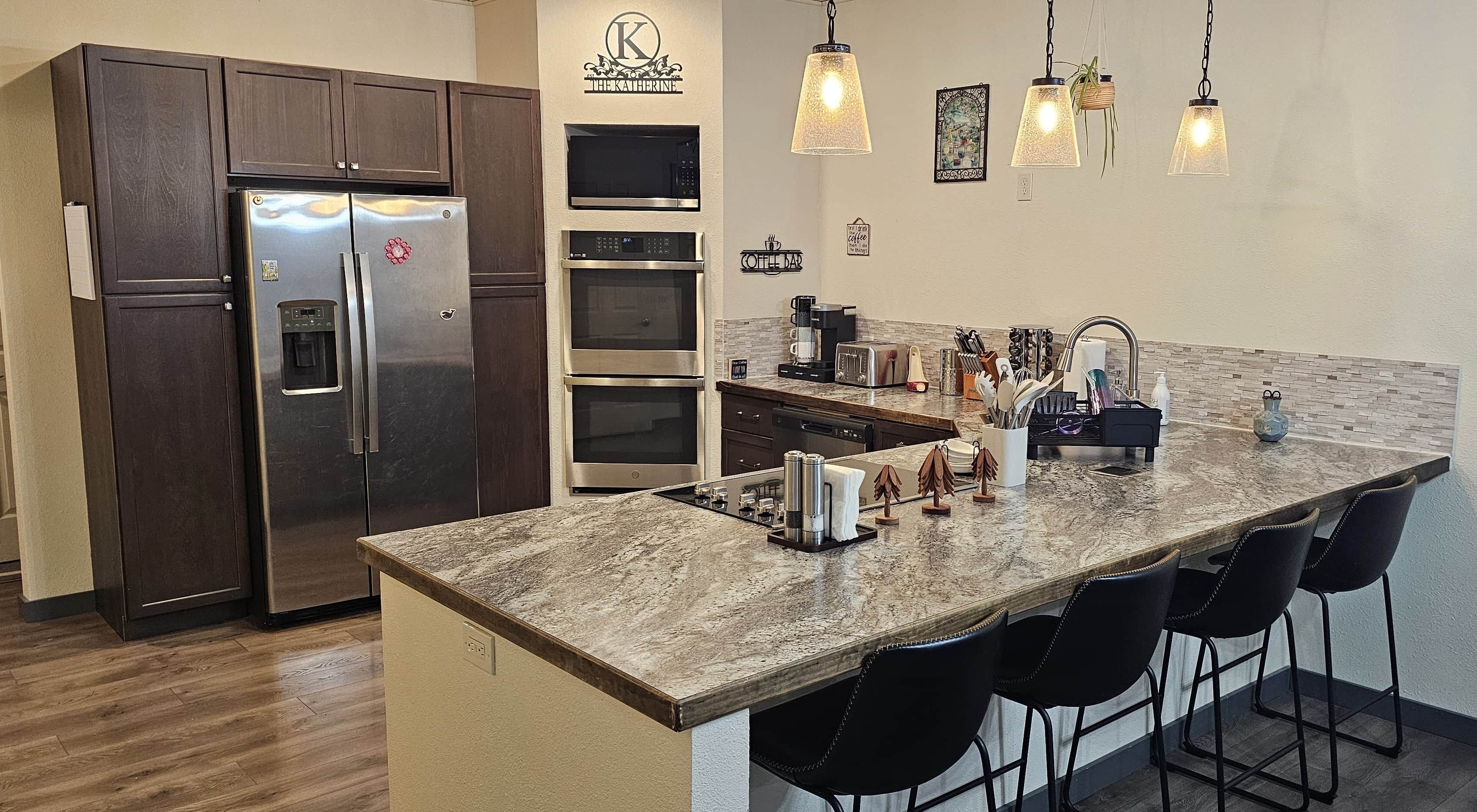 Una cocina moderna con una isla grande, electrodomésticos de acero inoxidable, lámparas colgantes y una barra para café.