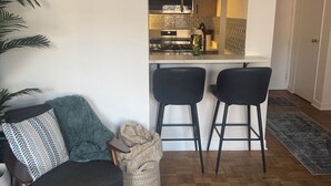 Ett vardagsrum med en soffa, en mönstrad matta och en köksdel med en spis och barstolar.