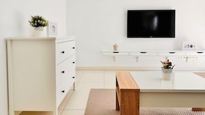 Uma sala de estar moderna com um armário branco, uma TV de tela plana na parede, um banco de madeira e uma pequena mesa com objetos decorativos.