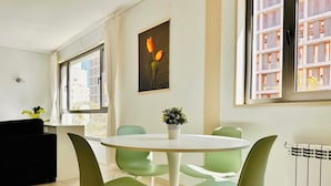 Uma sala de jantar moderna com uma mesa redonda, cadeiras verdes, uma planta em vaso e uma pintura de tulipas.