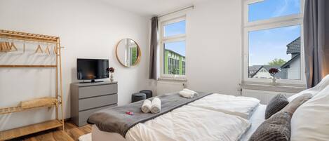 A bedroom with two beds, a TV, a mirror, a window, and a wooden drying rack.