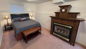 Un dormitorio con cama, lámparas de noche, un banco de madera, chimenea y un reloj.