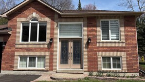 Una casa de dos pisos con fachada de ladrillo, puerta principal con panel de vidrio y varias ventanas.