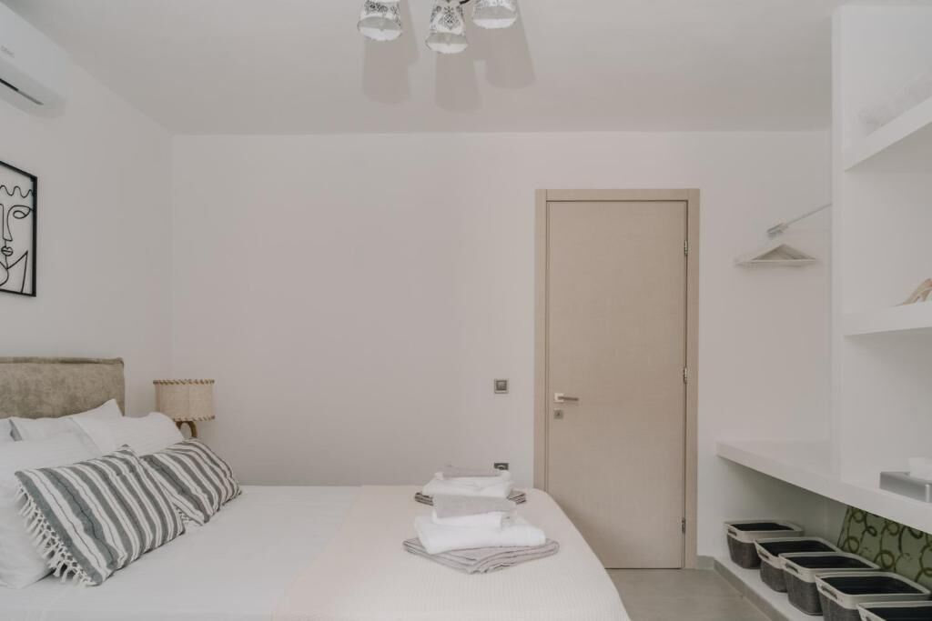 Quarto com cama, porta, luminária na parede e caixas organizadoras.