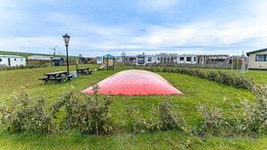 A grassy area with picnic tables, a playground, and mobile homes in the background. - Serene Waterfront Escape With Sauna (Stavenisse)