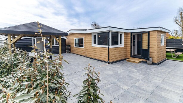 A modern, two-story wooden house with large windows and a covered patio area. - Serene Waterfront Escape With Sauna (Stavenisse)