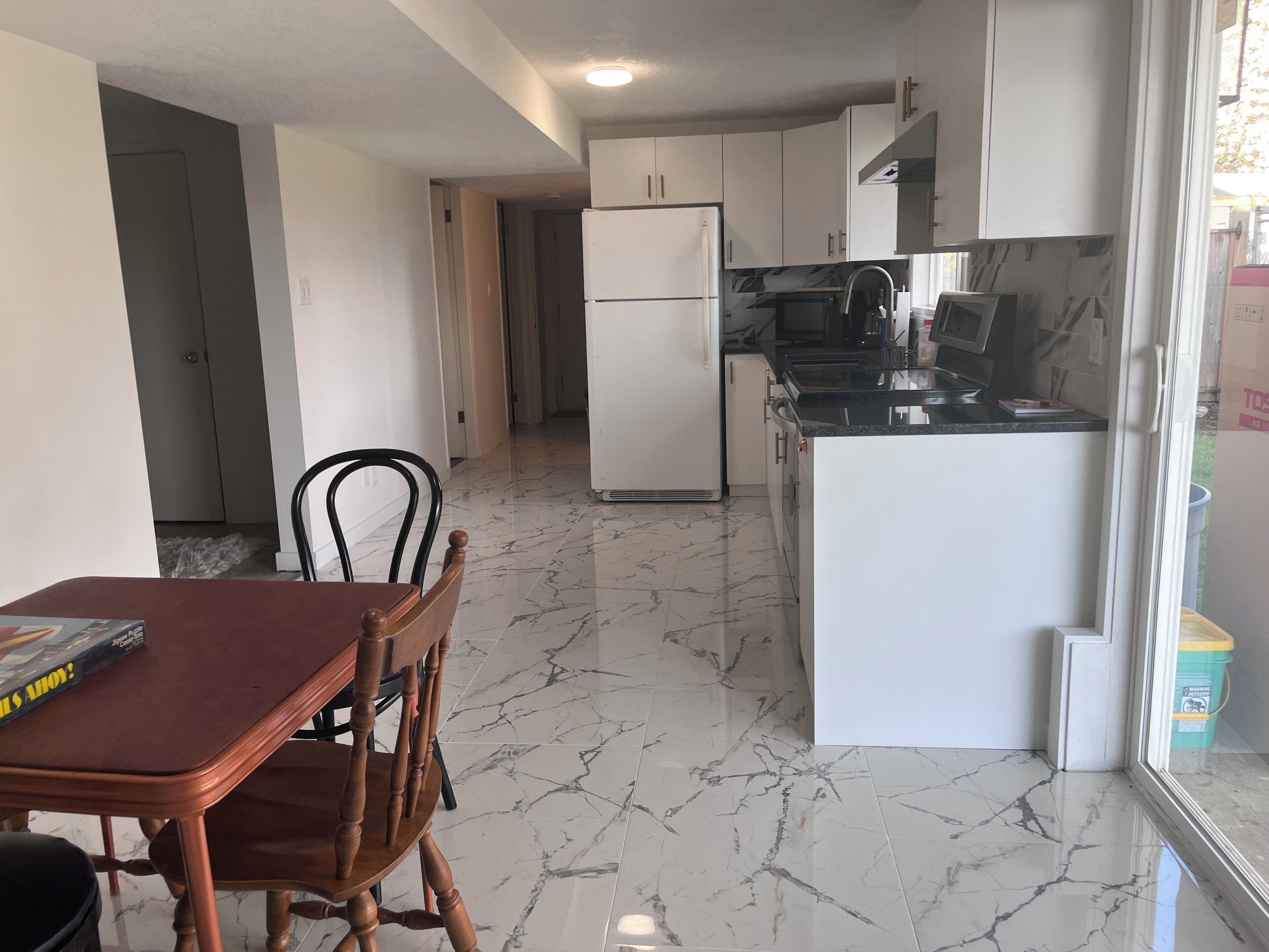 A kitchen with white cabinets, a black countertop, and a marble floor.