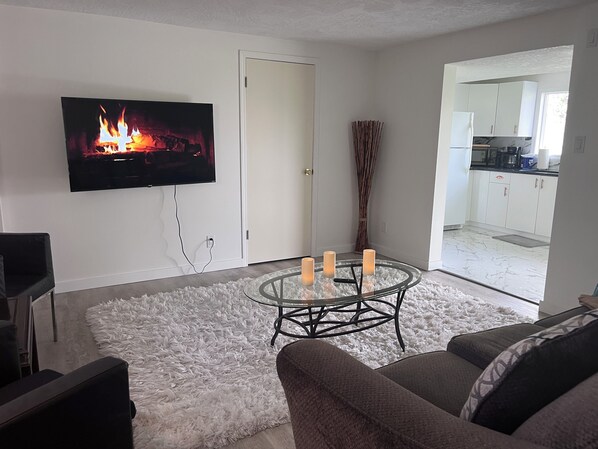 A living room with a TV, a round glass coffee table with candles, a fluffy rug, and a sofa.