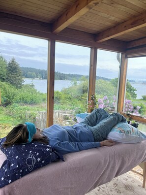 A person lying on a bed with a view of a lake and forest. - Ocean Lagoon Views - Steps to Water & Pet Friendly (Victoria)