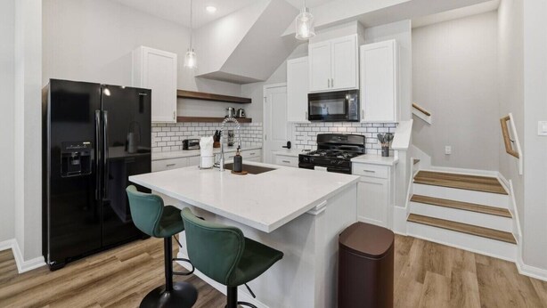Una cocina moderna con armarios blancos, un refrigerador negro, una isla central con taburetes de bar, un microondas y una estufa.