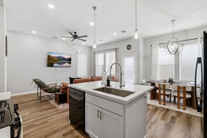 A modern kitchen with a central island, a dining area with a table and chairs, a sofa, and a ceiling fan. - Unwind & Relax 20 min to Downtown HOU! (Houston)