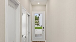Un pasillo con puertas blancas, piso de madera y vista a una casa a través de un vidrio.