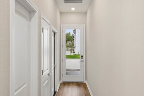 A hallway with white doors, a wooden floor, and a view of a house through a glass door. - Unwind & Relax 20 min to Downtown HOU! (Houston)