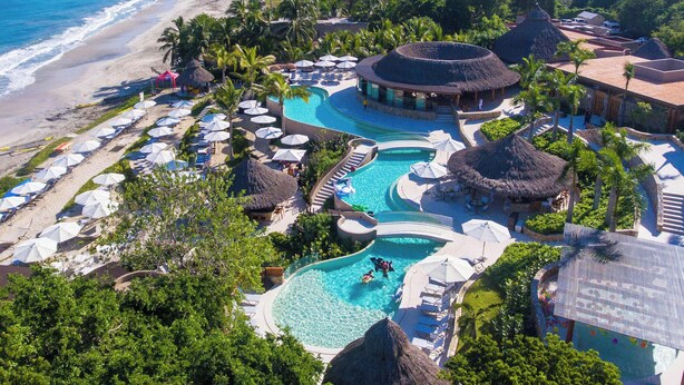 Resort com uma piscina grande, guarda-sóis e uma praia.