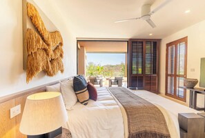 Ein modernes Schlafzimmer mit Bett, Lampe, Wandkunst und Blick ins Freie.