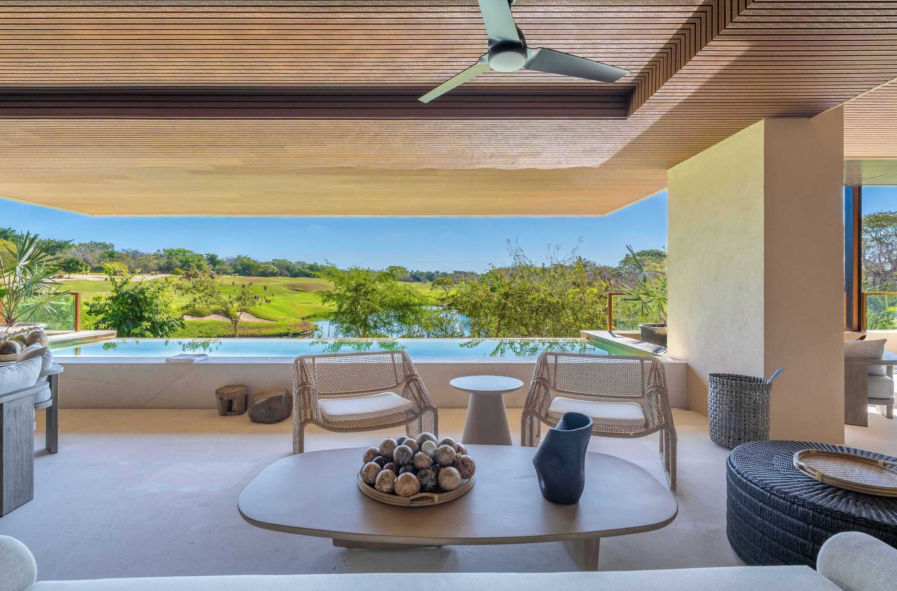 Un espace extérieur moderne, aménagé avec des meubles en osier, une table ronde ornée d’un récipient rempli de pierres, et offrant une vue sur un terrain de golf et une piscine.