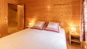 Ein Zimmer mit Holzwandverkleidung, einem Bett, zwei Nachttischlampen und einer Tür zu einem anderen Raum.