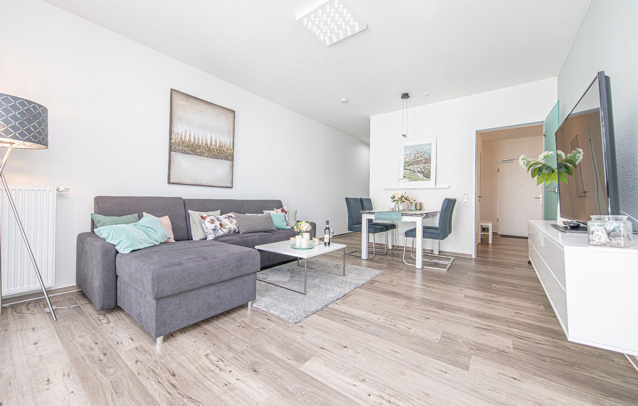 A modern living room with a grey sofa, a coffee table, and a dining area with a table and chairs.