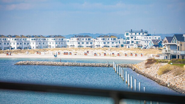 Ein Küstenhotel mit mehrstöckigen Gebäuden, einem Sandstrand und einem Felssteg.