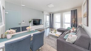 Ein modernes Wohnzimmer mit Flachbildfernseher, grauem Sofa, Esstisch und Stühlen.