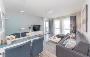 Ein modernes Wohnzimmer mit Flachbildfernseher, grauem Sofa, Esstisch und Stühlen.