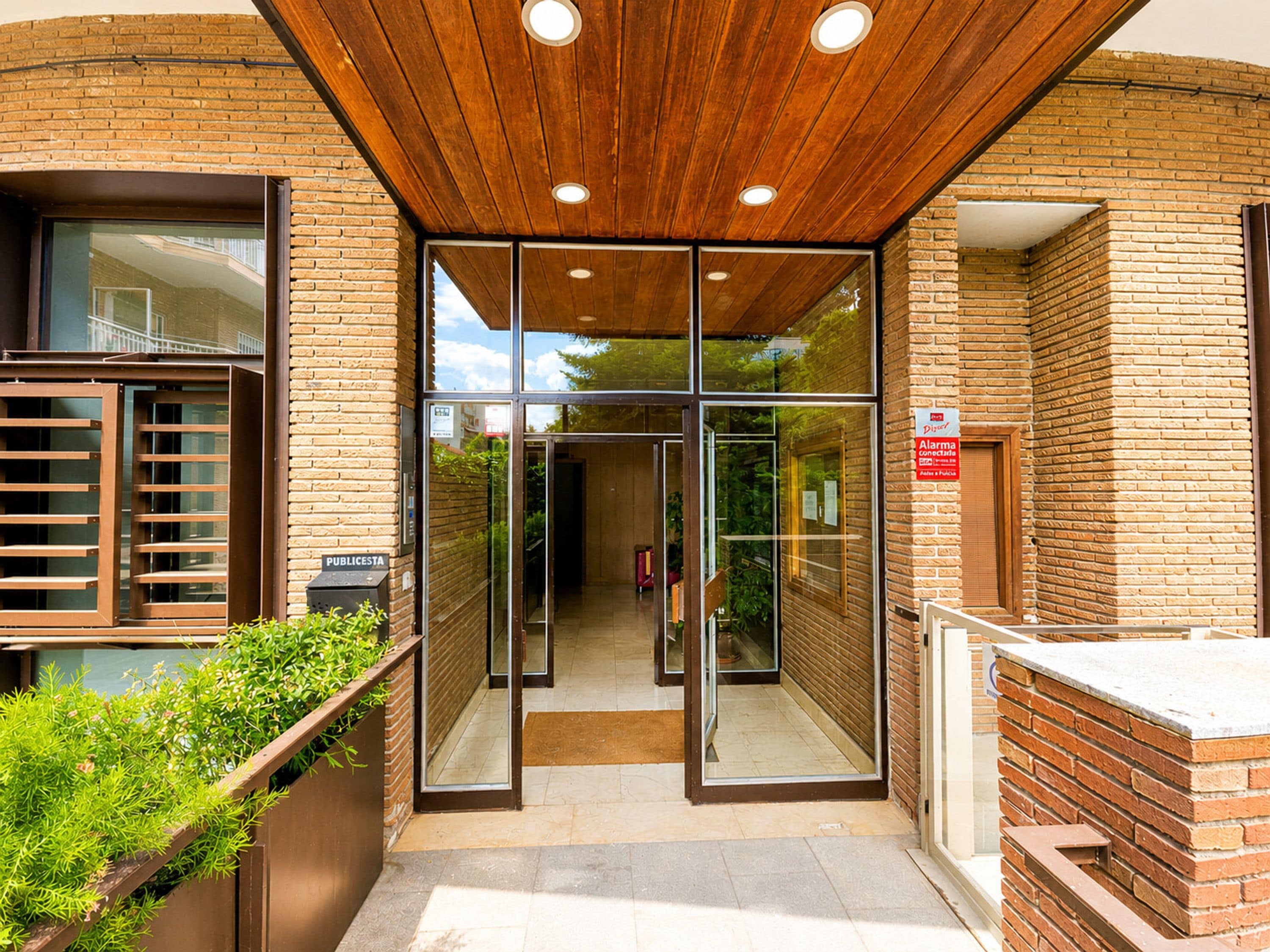 A building entrance with a glass door, a wooden ceiling, and a brick wall.