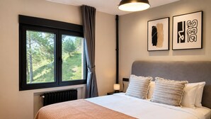 Un dormitorio con una cama grande, una ventana con cortinas, un radiador y dos cuadros en la pared.