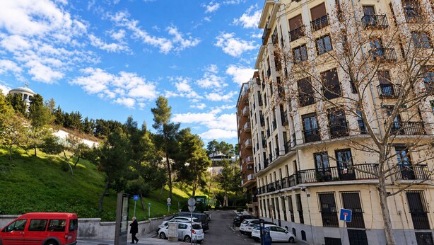 Un edificio residencial de varios pisos con balcones, autos estacionados y una vereda.
