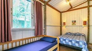 Une chambre individuelle avec un lit superposé en bois, une fenêtre avec des rideaux et un luminaire fixé au mur.